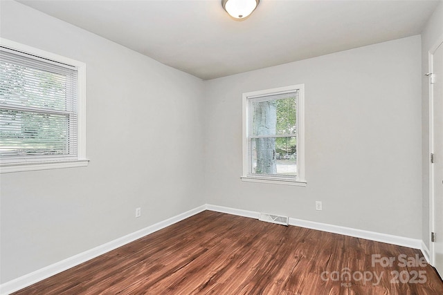 spare room featuring visible vents, baseboards, and dark wood-type flooring