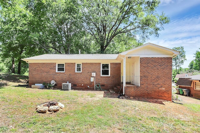 rear view of property with central AC unit, a yard, brick siding, and a fire pit