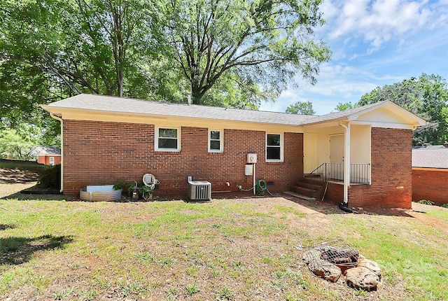 back of house with a yard, cooling unit, brick siding, and a fire pit