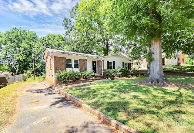 ranch-style house featuring fence, a front lawn, brick siding, and driveway