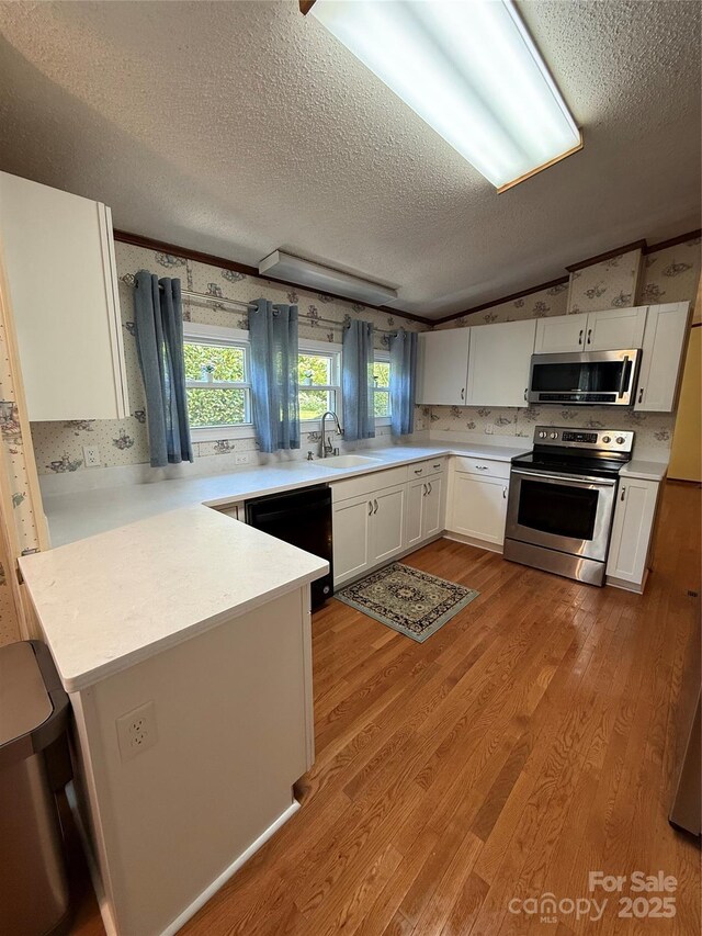 kitchen featuring stainless steel appliances, a textured ceiling, a peninsula, light countertops, and a sink