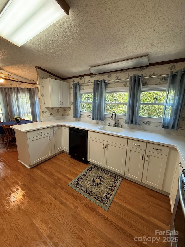 kitchen with a sink, dishwasher, a textured ceiling, a peninsula, and light wood-style flooring
