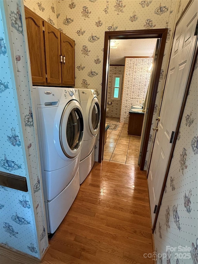 washroom with wallpapered walls, light wood-style floors, independent washer and dryer, and cabinet space