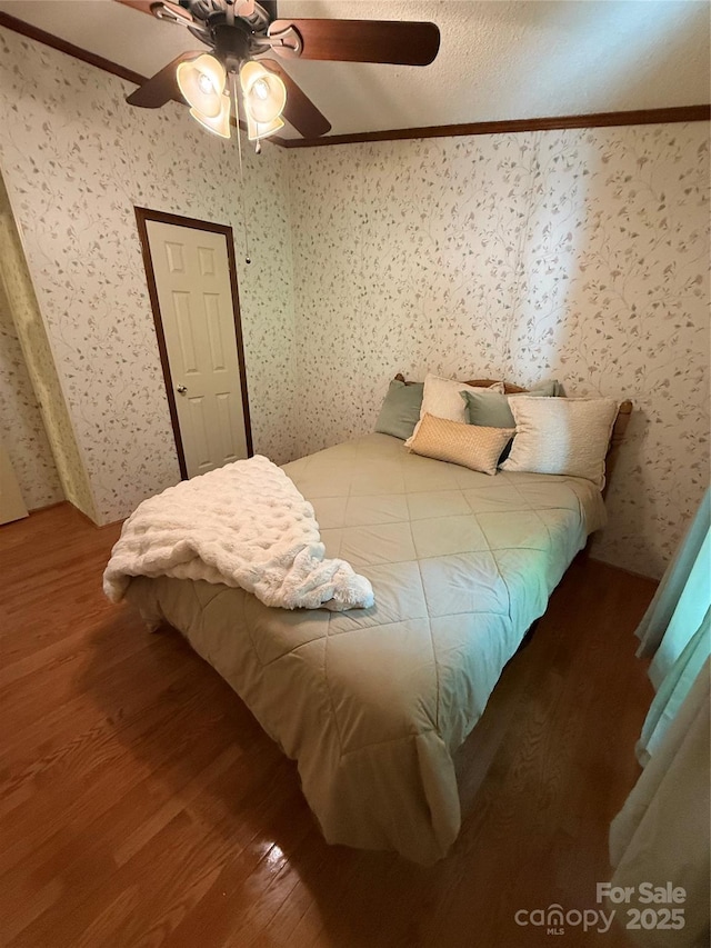 bedroom with wood finished floors, ornamental molding, wallpapered walls, and a ceiling fan