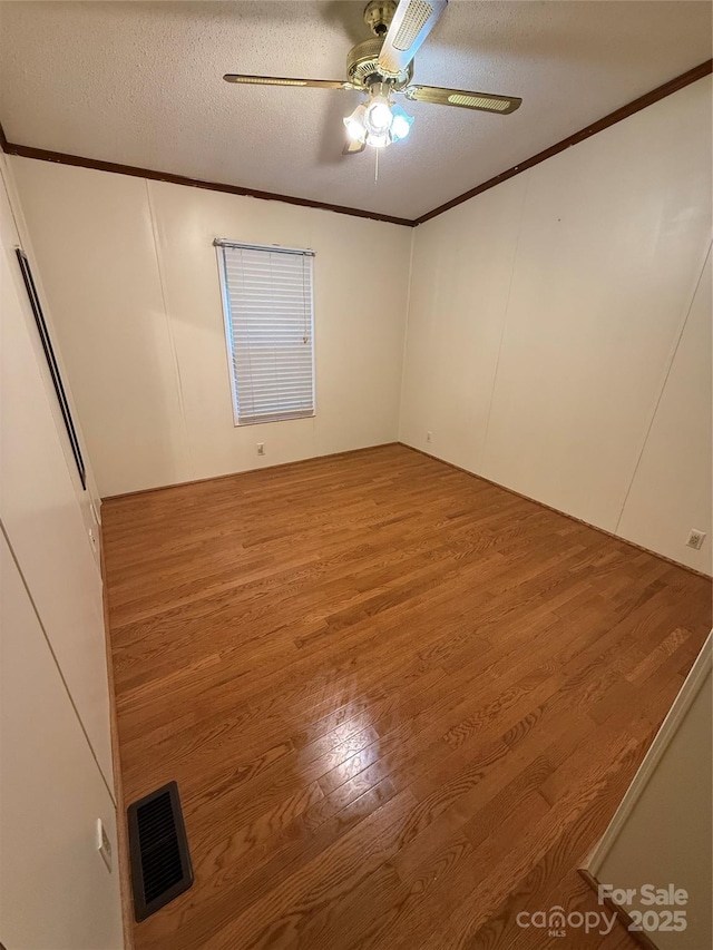 empty room featuring crown molding, wood finished floors, ceiling fan, and a textured ceiling