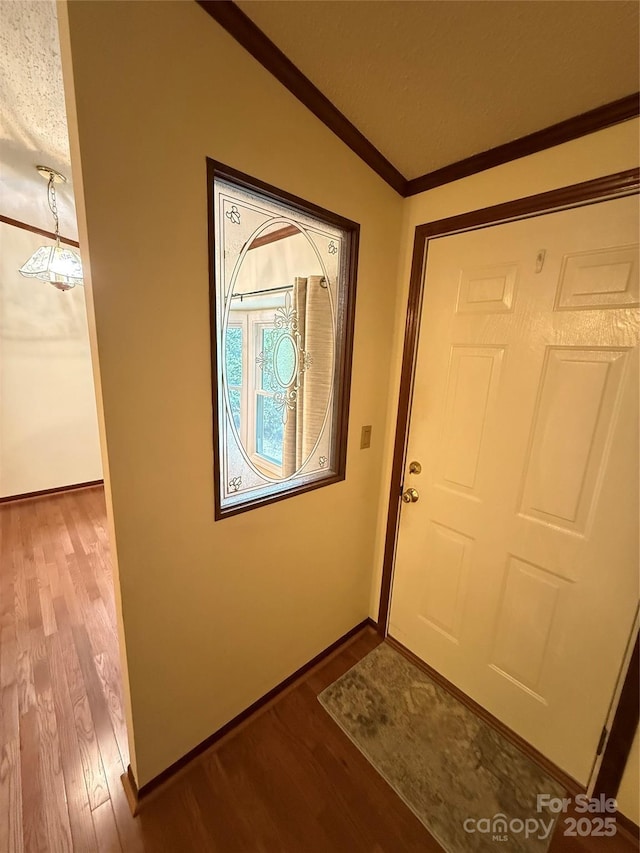entryway featuring wood finished floors, lofted ceiling, baseboards, and ornamental molding