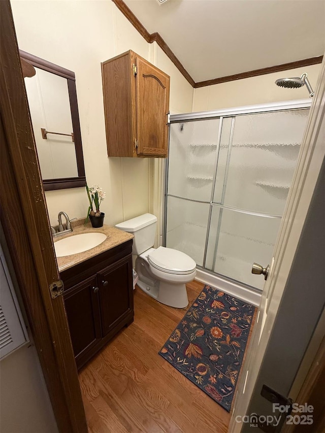 bathroom with wood finished floors, a stall shower, toilet, vanity, and ornamental molding