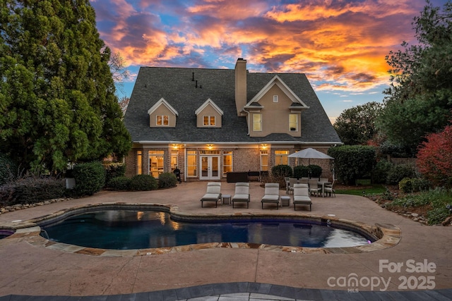 18823 Peninsula Cove Ln, Cornelius, NC 28031 - back of house at dusk featuring french doors, a chimney, a patio area, an outdoor pool, and brick siding