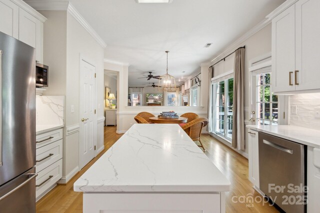 kitchen with stainless steel appliances, ornamental molding, light wood finished floors, white cabinets, and a kitchen island