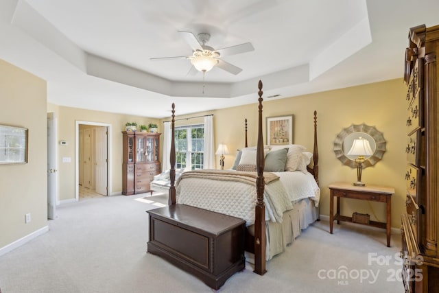 bedroom featuring light colored carpet, a tray ceiling, baseboards, and ceiling fan