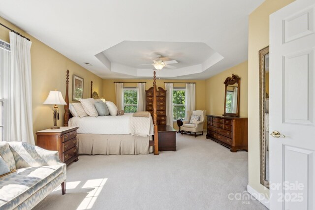 bedroom featuring a tray ceiling, light colored carpet, and a ceiling fan