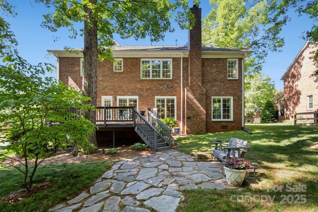 rear view of house featuring a patio area, a deck, brick siding, a chimney, and a lawn