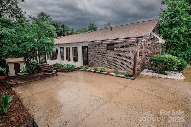 rear view of house featuring a patio, a storage shed, a shingled roof, brick siding, and an outdoor structure