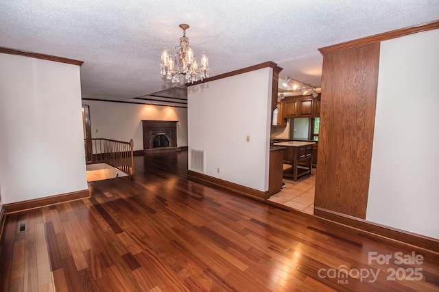 unfurnished living room featuring a textured ceiling, wood finished floors, ornamental molding, baseboards, and a chandelier