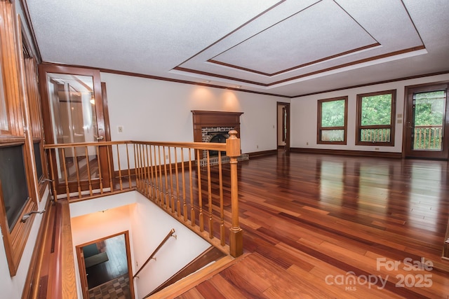 empty room featuring a tray ceiling, a brick fireplace, wood finished floors, crown molding, and baseboards