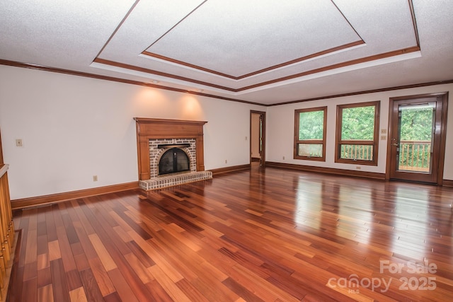 unfurnished living room featuring a raised ceiling, a fireplace, wood finished floors, ornamental molding, and a textured ceiling