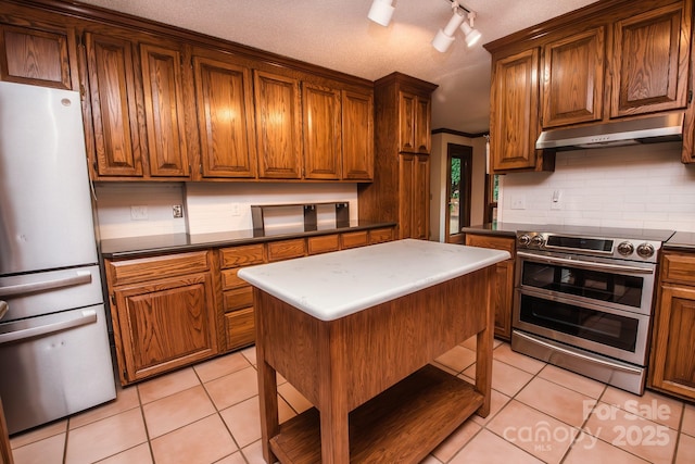 kitchen with freestanding refrigerator, double oven range, under cabinet range hood, light tile patterned flooring, and backsplash
