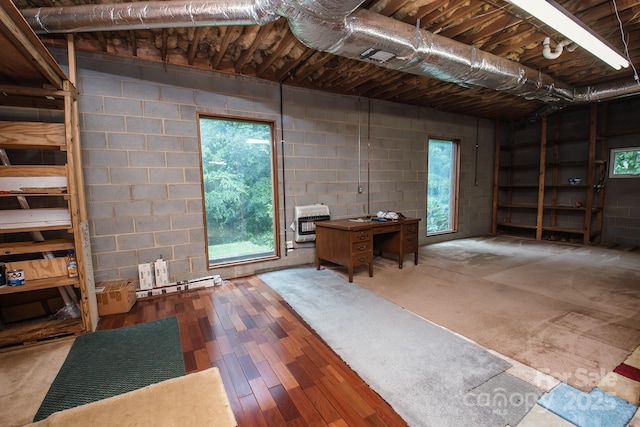 below grade area featuring heating unit, wood finished floors, and concrete block wall
