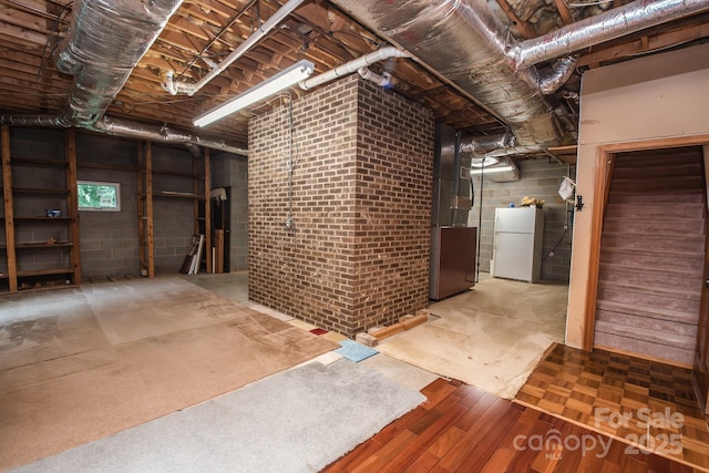 unfinished basement with freestanding refrigerator, concrete block wall, heating unit, and wood finished floors