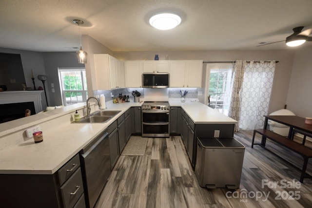 kitchen with a sink, a peninsula, wood finished floors, light countertops, and appliances with stainless steel finishes
