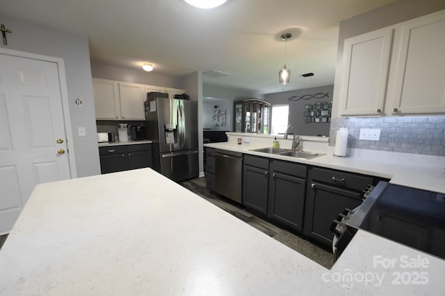 kitchen featuring a sink, stainless steel appliances, tasteful backsplash, light countertops, and hanging light fixtures