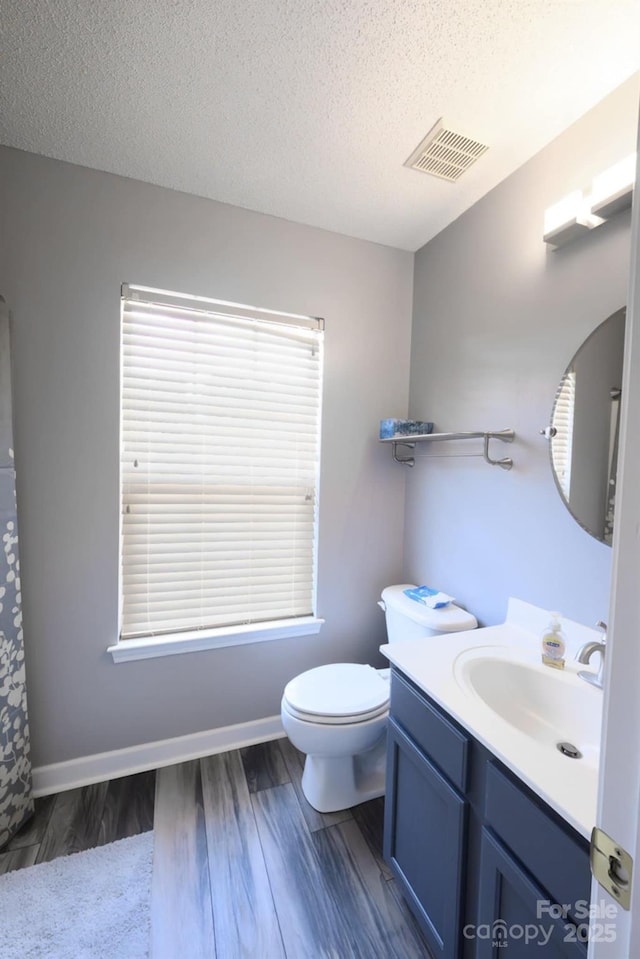 bathroom featuring toilet, wood finished floors, a textured ceiling, visible vents, and vanity