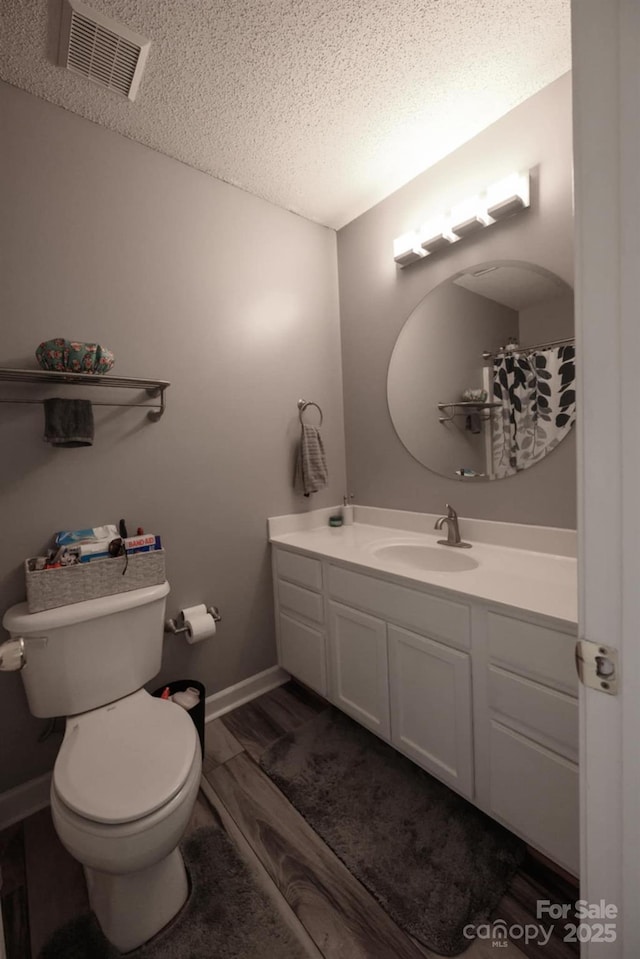 bathroom with a textured ceiling, toilet, baseboards, visible vents, and vanity