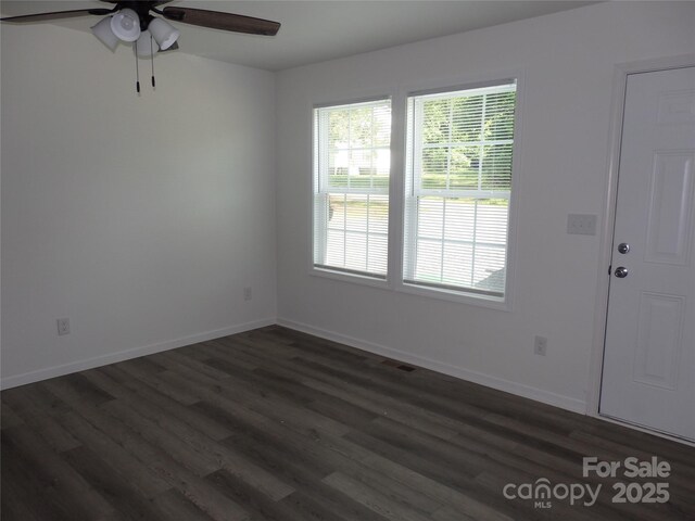 spare room featuring a ceiling fan, dark wood finished floors, and baseboards