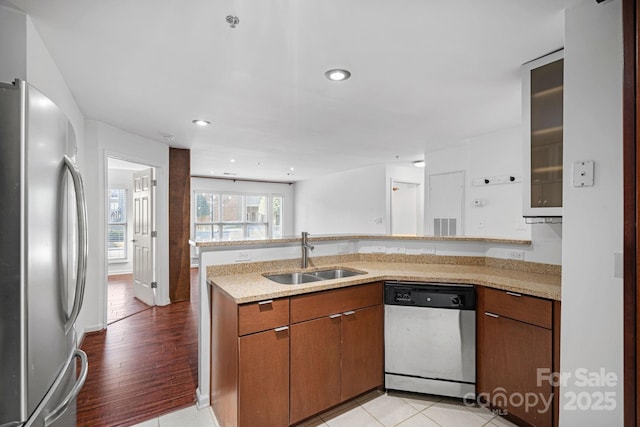 kitchen featuring stainless steel appliances, a sink, a peninsula, brown cabinetry, and recessed lighting