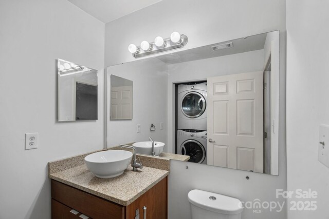 bathroom with stacked washer / drying machine, toilet, and vanity