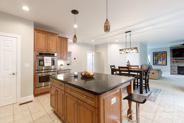 kitchen with stainless steel double oven, brown cabinetry, visible vents, a kitchen island, and light tile patterned flooring