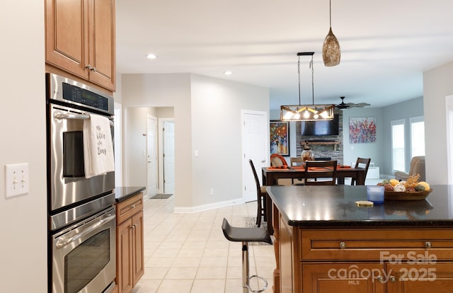 kitchen featuring brown cabinetry, dark countertops, hanging light fixtures, and stainless steel double oven