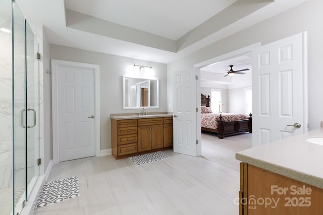 bathroom featuring a ceiling fan, connected bathroom, vanity, a marble finish shower, and a raised ceiling