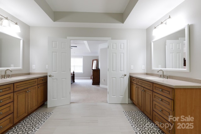 full bath with a raised ceiling, two vanities, and a sink