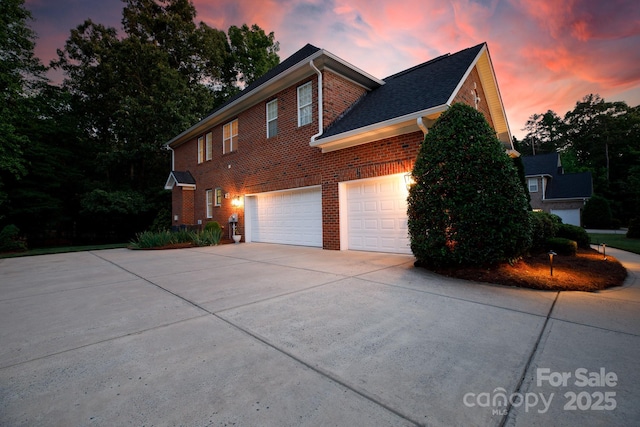 property exterior at dusk with concrete driveway, an attached garage, and brick siding
