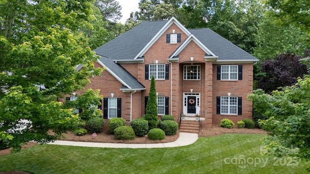 colonial-style house with a shingled roof, brick siding, and a front yard