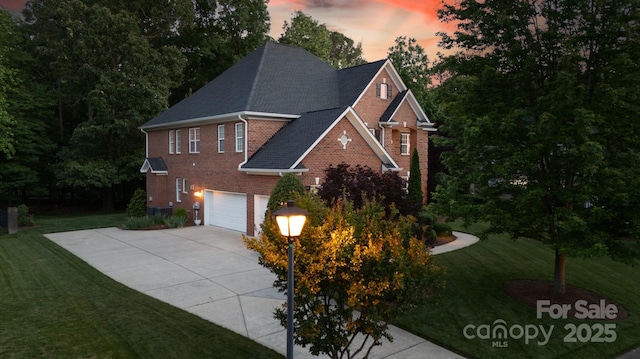 traditional-style house featuring a yard, brick siding, a garage, a shingled roof, and concrete driveway