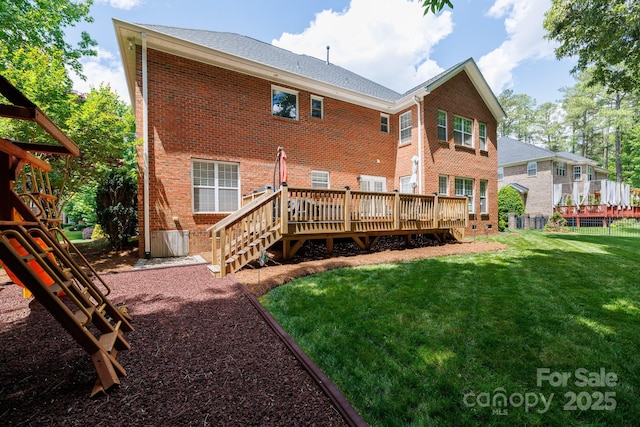 rear view of property featuring brick siding, a wooden deck, fence, and a lawn