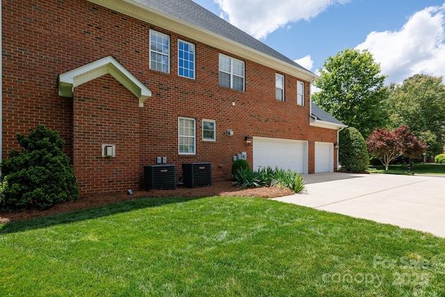 view of side of home featuring central air condition unit, driveway, brick siding, and a yard