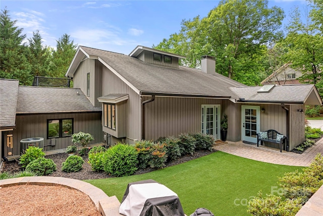 back of property featuring a chimney, roof with shingles, a yard, central air condition unit, and a patio area