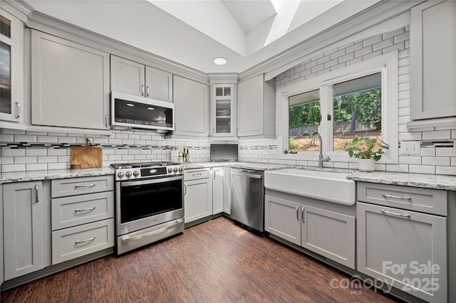 kitchen with appliances with stainless steel finishes, gray cabinets, lofted ceiling, tasteful backsplash, and a sink