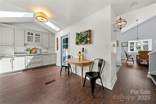 dining space with a skylight, lofted ceiling, dark wood-type flooring, baseboards, and a chandelier