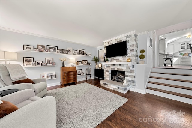 living area featuring dark wood-style floors, a stone fireplace, crown molding, and baseboards