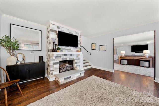 living room featuring crown molding, hardwood / wood-style floors, baseboards, stairs, and a stone fireplace