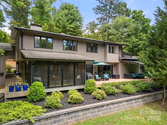 rear view of property featuring a sunroom, a patio, an outdoor living space, a chimney, and a shingled roof
