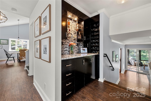 indoor wet bar featuring baseboards, tasteful backsplash, dark wood-style floors, crown molding, and hanging light fixtures