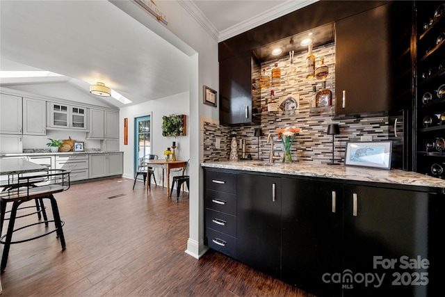 bar area featuring a sink, decorative backsplash, dark wood-style floors, crown molding, and vaulted ceiling
