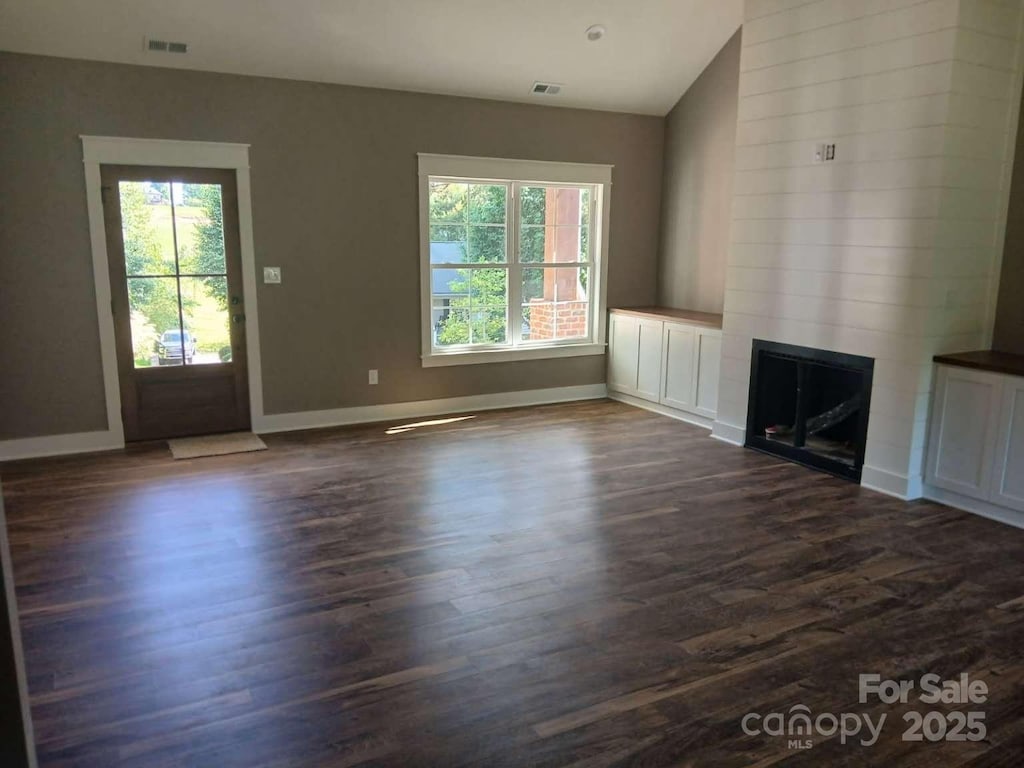 unfurnished living room with baseboards, dark wood finished floors, visible vents, and a large fireplace