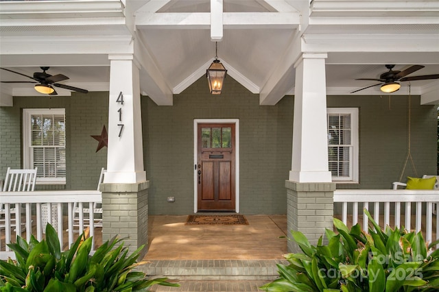 view of exterior entry with ceiling fan, a porch, and brick siding