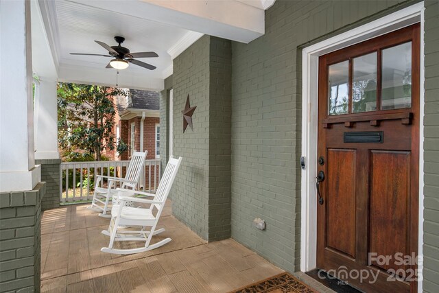 view of exterior entry with a porch, brick siding, and ceiling fan